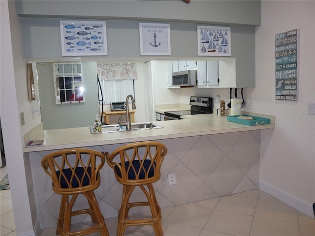 kitchen featuring sink, light tile patterned flooring, a kitchen bar, white cabinets, and appliances with stainless steel finishes