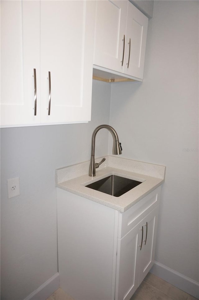 kitchen featuring white cabinets, light stone counters, tile patterned floors, and sink