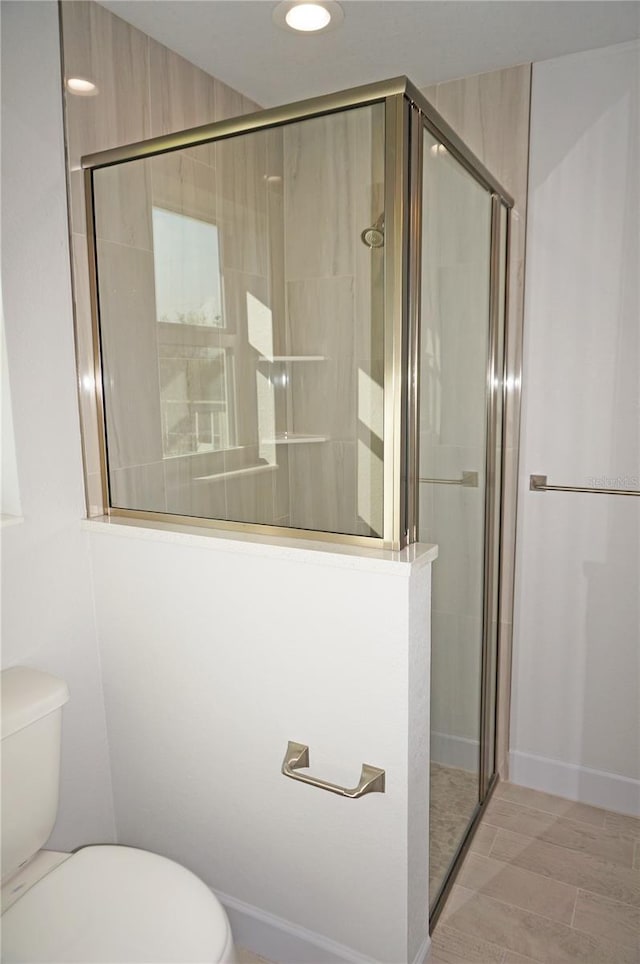 bathroom featuring a shower with door and toilet