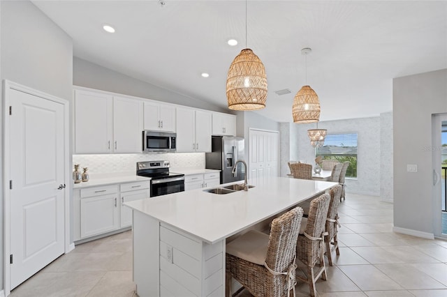 kitchen with decorative light fixtures, lofted ceiling, sink, a kitchen island with sink, and stainless steel appliances