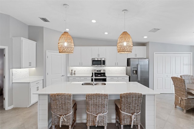 kitchen featuring appliances with stainless steel finishes, hanging light fixtures, a center island with sink, decorative backsplash, and vaulted ceiling