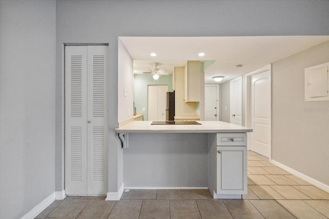 kitchen featuring a breakfast bar, ceiling fan, light tile patterned floors, kitchen peninsula, and stainless steel refrigerator