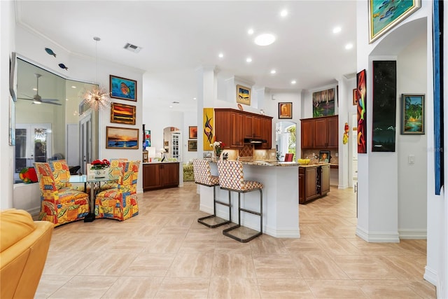 kitchen featuring ceiling fan, light stone counters, backsplash, kitchen peninsula, and a breakfast bar area