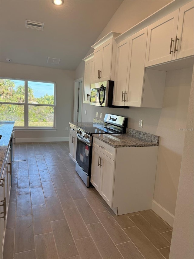 kitchen featuring visible vents, lofted ceiling, appliances with stainless steel finishes, dark stone countertops, and white cabinetry