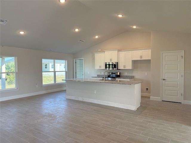 kitchen with light wood-style flooring, appliances with stainless steel finishes, white cabinetry, a sink, and light stone countertops