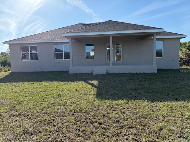 back of house with roof with shingles, a lawn, and stucco siding