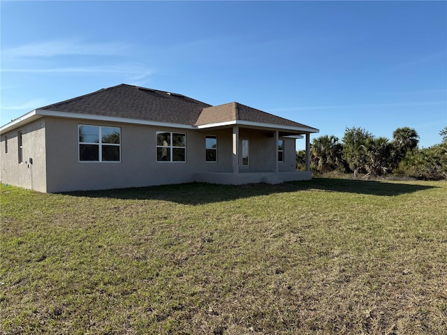 rear view of house with roof with shingles, a yard, and stucco siding