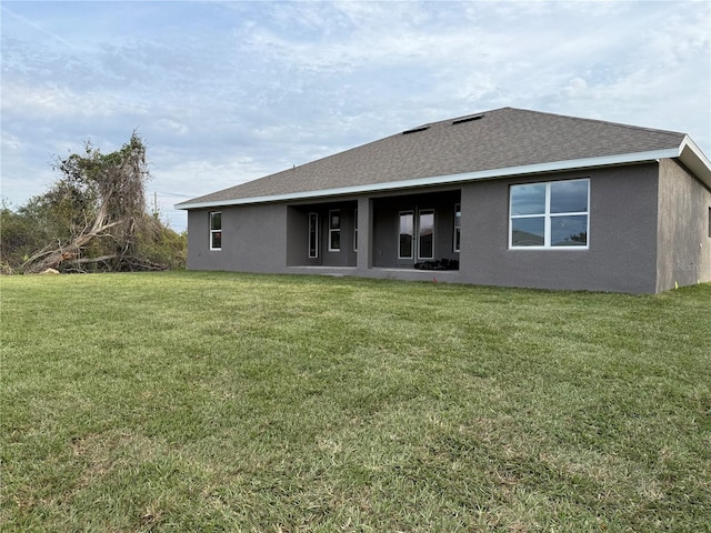 rear view of property featuring roof with shingles, a lawn, and stucco siding