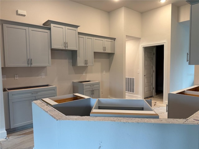 kitchen with a peninsula, light wood-style floors, visible vents, and gray cabinetry