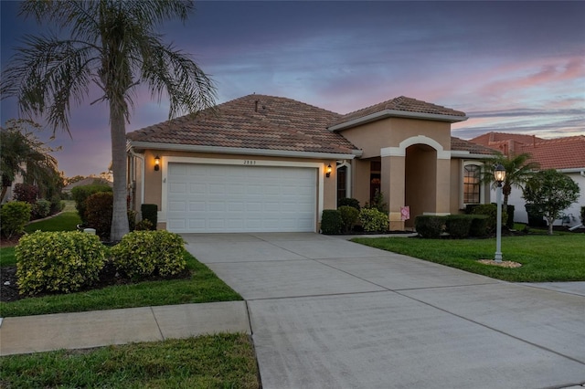 mediterranean / spanish-style house featuring concrete driveway, a lawn, a tiled roof, an attached garage, and stucco siding