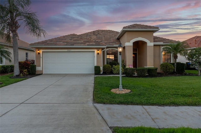 mediterranean / spanish house with stucco siding, a front lawn, concrete driveway, a garage, and a tiled roof