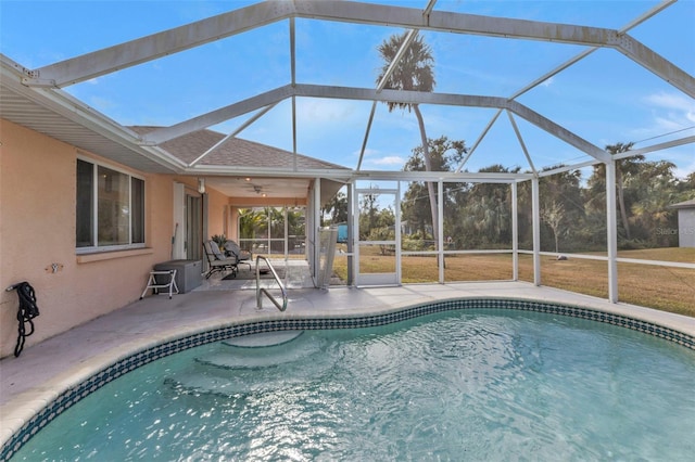 view of swimming pool featuring glass enclosure, ceiling fan, a yard, and a patio