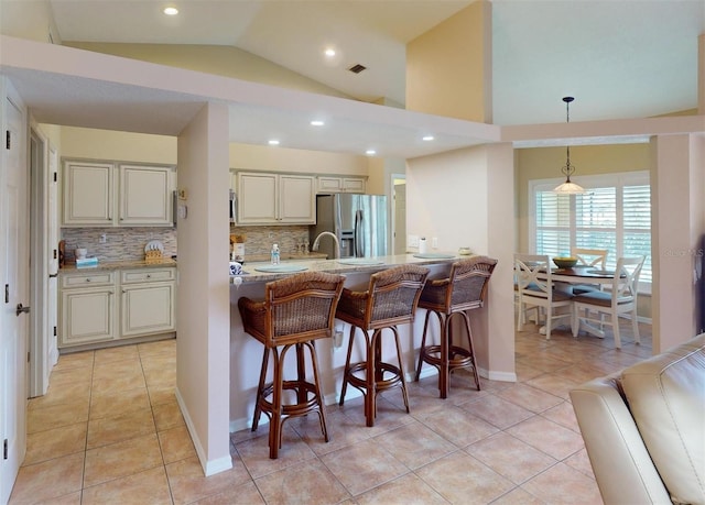 kitchen with hanging light fixtures, tasteful backsplash, stainless steel fridge, vaulted ceiling, and light tile patterned floors