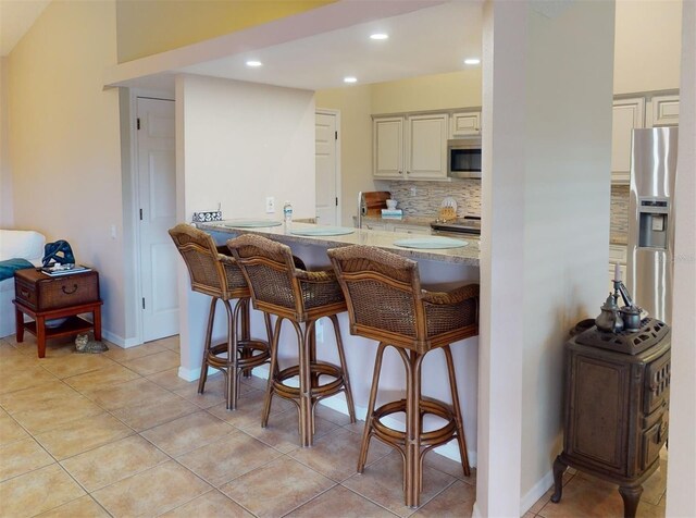 kitchen featuring decorative backsplash, appliances with stainless steel finishes, kitchen peninsula, and a kitchen breakfast bar