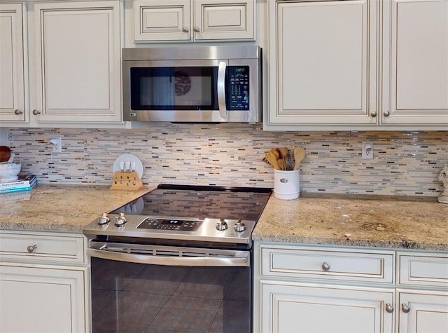 kitchen featuring light stone countertops, backsplash, stainless steel appliances, and white cabinetry