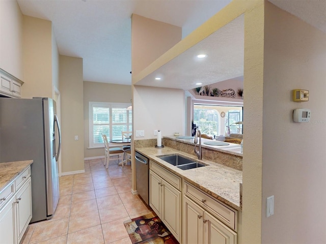 kitchen with light stone countertops, sink, cream cabinetry, light tile patterned floors, and appliances with stainless steel finishes