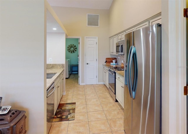 kitchen with light stone counters, stainless steel appliances, sink, cream cabinetry, and light tile patterned flooring