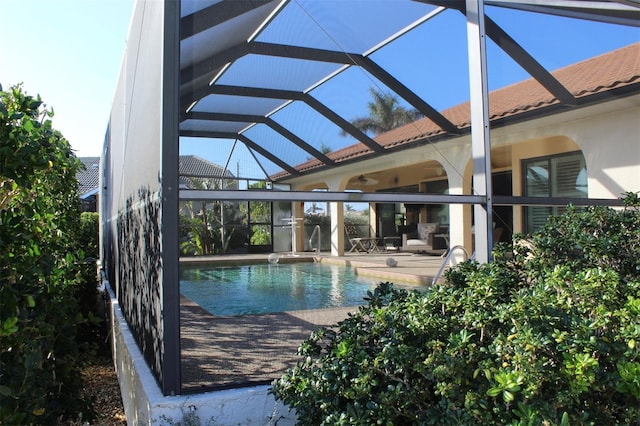 view of swimming pool with glass enclosure, ceiling fan, and a patio area