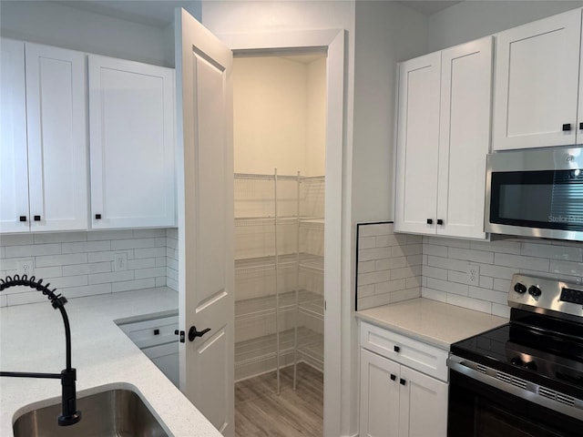 kitchen with white cabinets, sink, decorative backsplash, light hardwood / wood-style floors, and stainless steel appliances