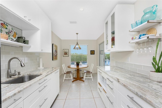 kitchen featuring tasteful backsplash, light stone counters, sink, white cabinets, and light tile patterned flooring