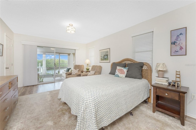 bedroom featuring access to exterior, a textured ceiling, and light wood-type flooring