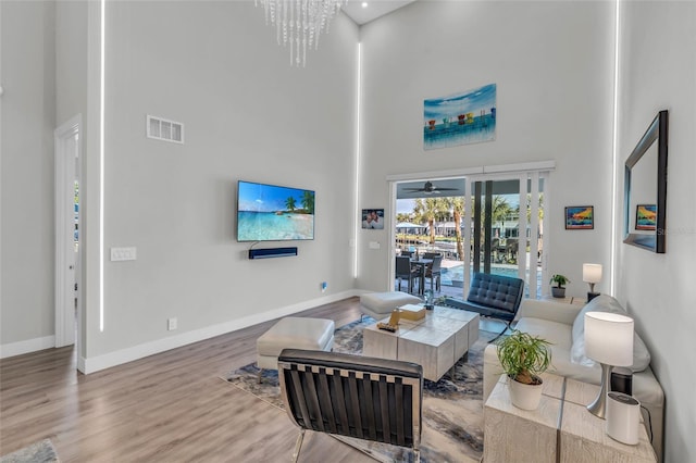 living room featuring ceiling fan with notable chandelier, hardwood / wood-style floors, and a towering ceiling