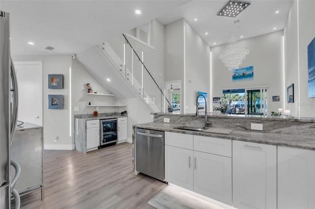 kitchen with light stone countertops, a towering ceiling, stainless steel appliances, sink, and white cabinets