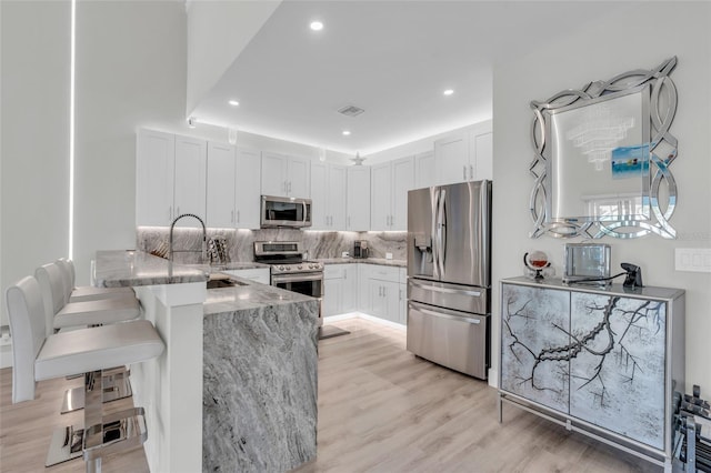 kitchen featuring kitchen peninsula, stainless steel appliances, white cabinetry, and light hardwood / wood-style flooring