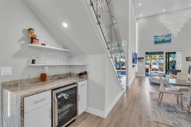 bar featuring high vaulted ceiling, light hardwood / wood-style flooring, light stone counters, white cabinetry, and beverage cooler