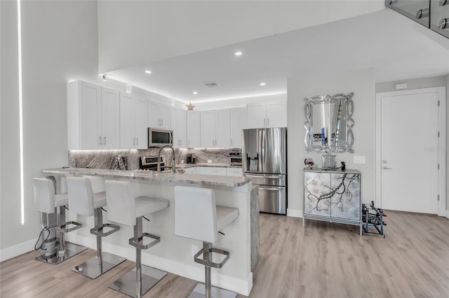 kitchen featuring appliances with stainless steel finishes, a kitchen breakfast bar, light stone counters, light hardwood / wood-style floors, and white cabinetry