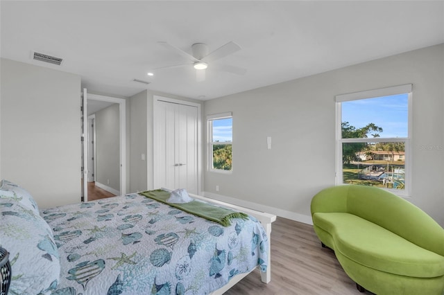 bedroom with multiple windows, light wood-type flooring, a closet, and ceiling fan