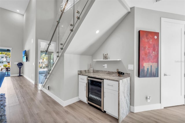 bar with white cabinets, light stone counters, light wood-type flooring, and wine cooler