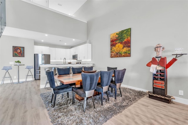 dining area featuring sink, a towering ceiling, and light hardwood / wood-style floors