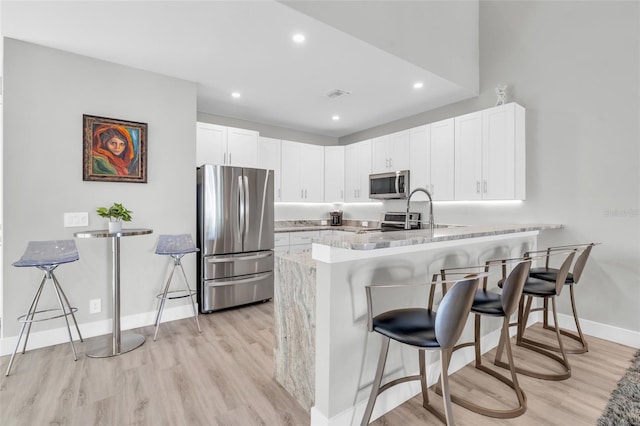 kitchen featuring kitchen peninsula, a kitchen bar, stainless steel appliances, and white cabinetry