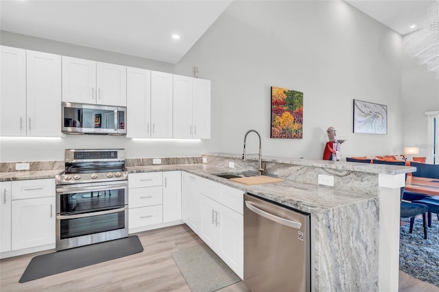 kitchen with kitchen peninsula, stainless steel appliances, sink, high vaulted ceiling, and white cabinets