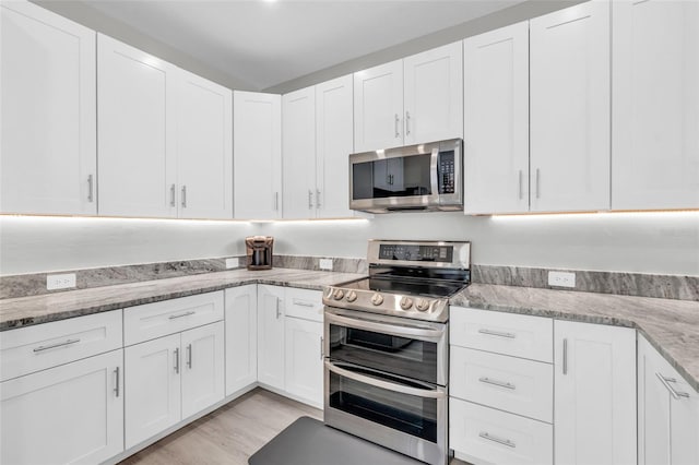 kitchen with light stone countertops, stainless steel appliances, white cabinetry, and light hardwood / wood-style floors