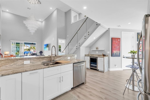 kitchen with light stone counters, stainless steel appliances, sink, white cabinetry, and wine cooler