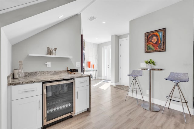 kitchen featuring stone counters, white cabinets, wine cooler, vaulted ceiling, and light hardwood / wood-style floors