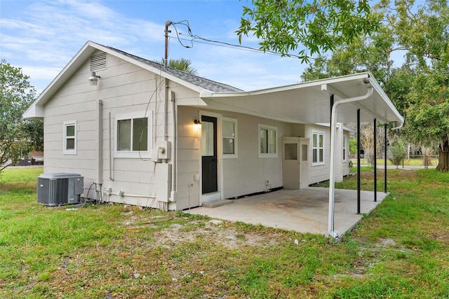 back of property featuring a carport, central AC unit, and a lawn