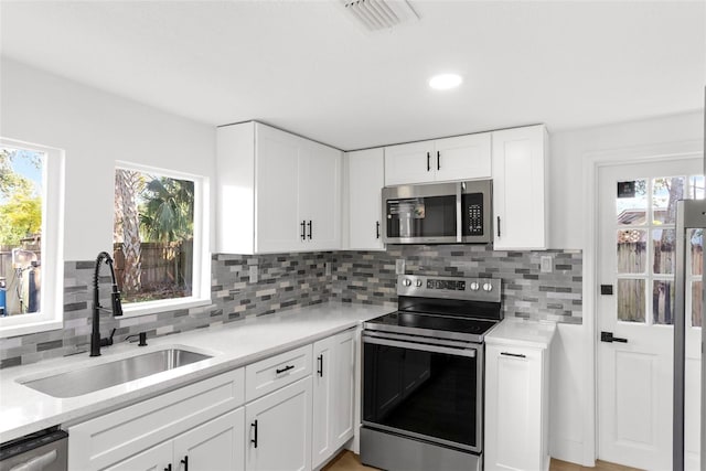 kitchen with decorative backsplash, appliances with stainless steel finishes, light stone counters, sink, and white cabinetry