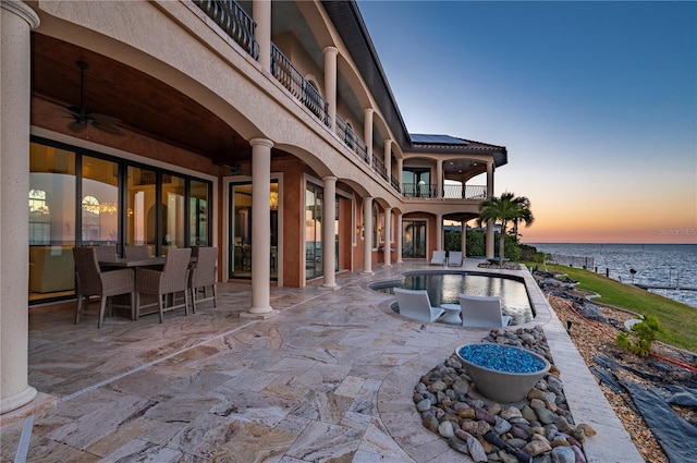 patio terrace at dusk with a water view and ceiling fan