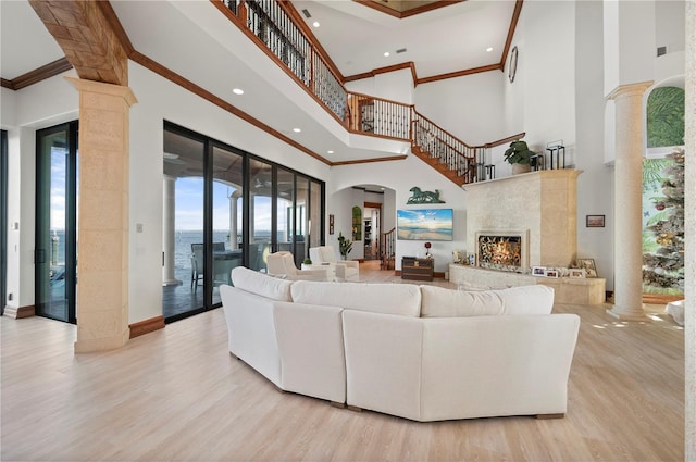 living room featuring light hardwood / wood-style floors, a towering ceiling, crown molding, and decorative columns