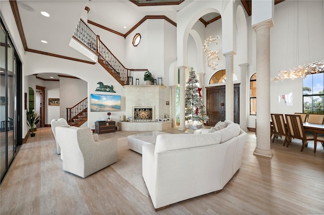 living room with light hardwood / wood-style floors, a towering ceiling, ornamental molding, and decorative columns