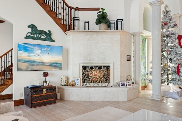 living room with hardwood / wood-style flooring, a tile fireplace, ornate columns, and a high ceiling