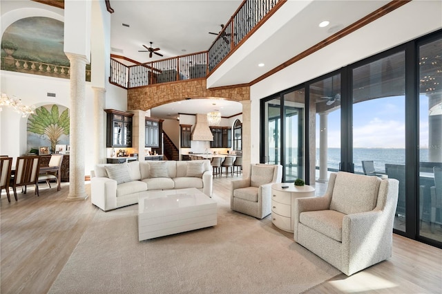 living room featuring ornate columns, light hardwood / wood-style flooring, a water view, and a high ceiling