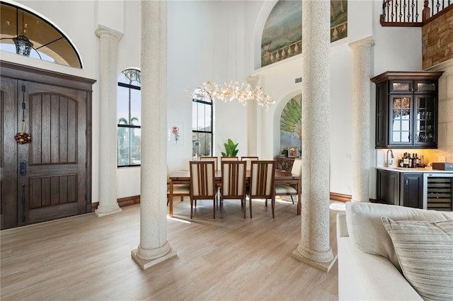 foyer featuring a towering ceiling, light hardwood / wood-style flooring, beverage cooler, and ornate columns