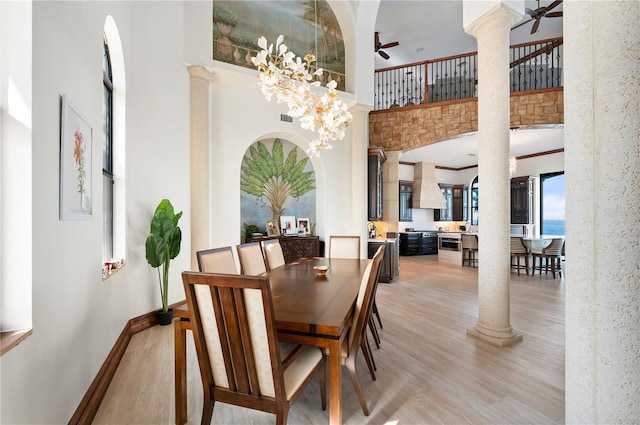 dining area featuring decorative columns, ceiling fan, light hardwood / wood-style flooring, and a towering ceiling