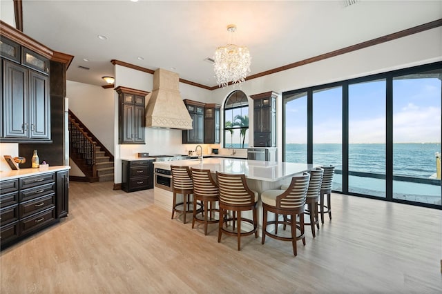 dining area featuring ornamental molding, light wood-type flooring, a water view, and a notable chandelier