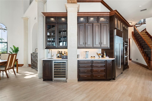 bar with light hardwood / wood-style floors, dark brown cabinetry, sink, and wine cooler