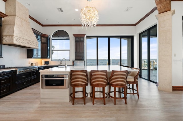 kitchen featuring hanging light fixtures, stainless steel appliances, light hardwood / wood-style flooring, a kitchen island with sink, and custom range hood